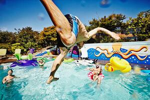 Umelecká fotografie Man in mid air jumping into pool during party, Thomas Barwick, (40 x 26.7 cm)