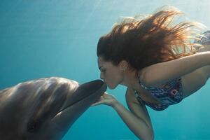 Fotografia Young Woman Kisses Dolphin Underwater, Sunbeams, Justin Lewis, (40 x 26.7 cm)