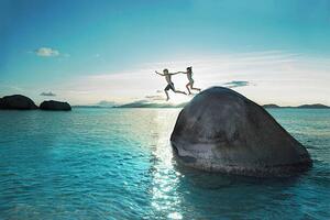 Umelecká fotografie Two kids holding hands jumping off rock into sea, Gary John Norman, (40 x 26.7 cm)