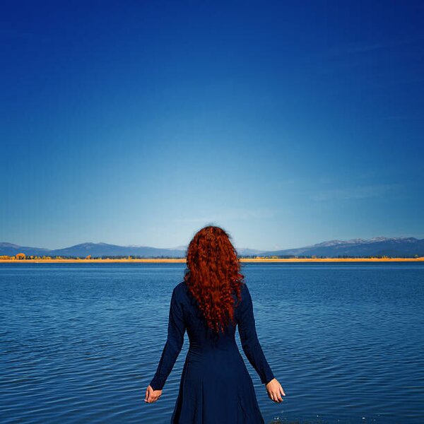 Umelecká fotografie Redhead in blue dress faces rippled lake, Anna Gorin, (40 x 40 cm)